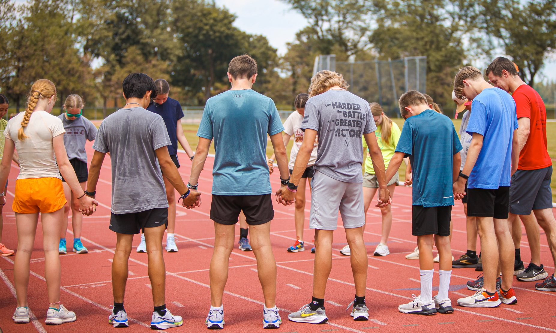 Athletes, runners, linking hands on a track after running club satellite at Summer Games, to pray before ending their time together for the day.